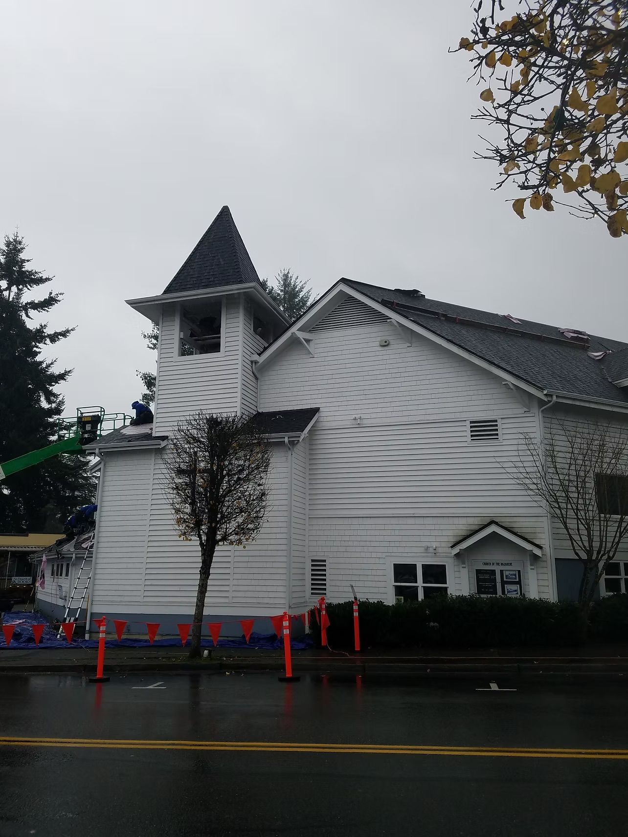 White church with steeple and cross beside a wet road on a rainy day, with traffic cones in front