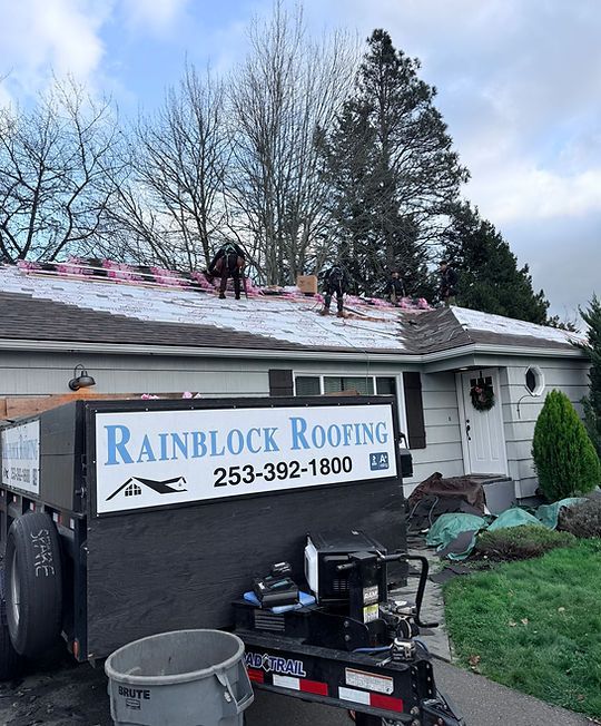 Rainblock Roofing crew repairing a roof on a house with a company sign and equipment below