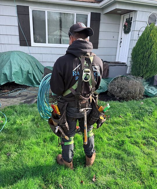 Person in climbing gear standing on grass in front of a house, viewed from behind.