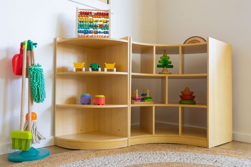 Toy wooden dollhouse with open shelves, small colorful toys, and cleaning tools on the left