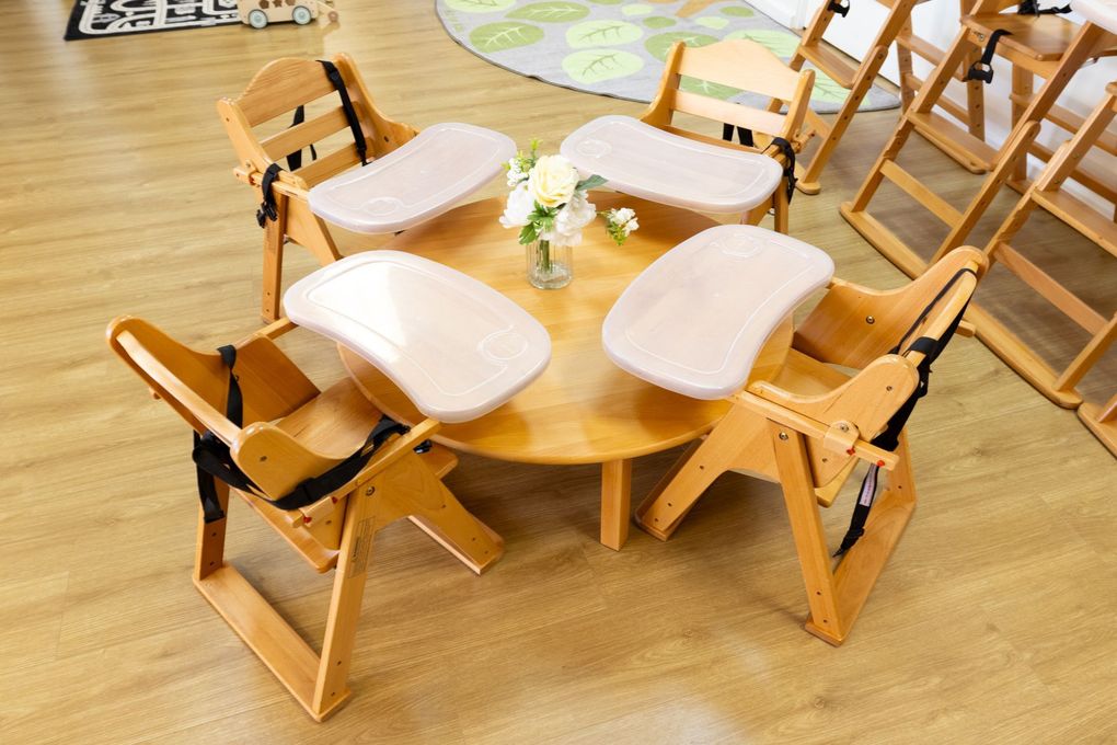 Round wooden kids' table with four small chairs and white cushions on a light wood floor