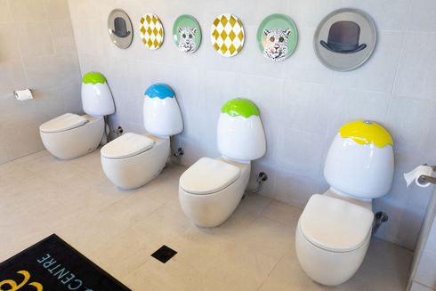 Row of colorful toilets in a clean restroom with cartoon-style wall decorations