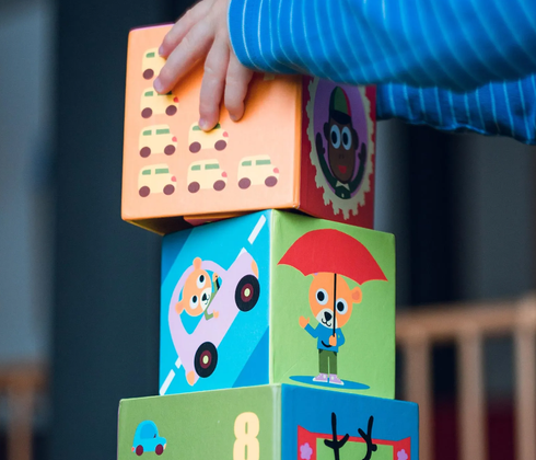 Hand stacking colorful toy blocks with cartoon faces outdoors