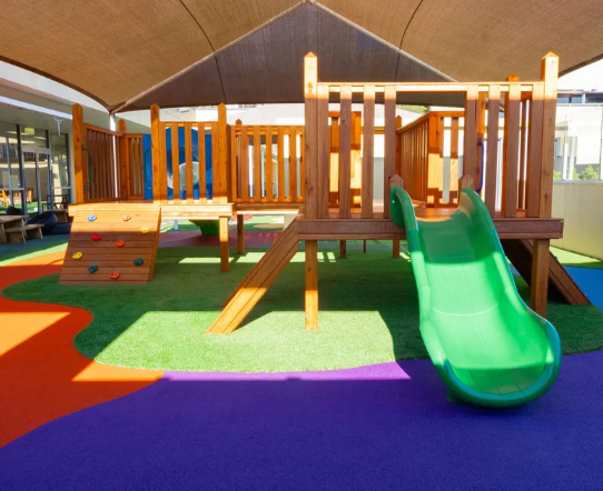 Colorful playground with slide, climbing platform, and padded flooring in bright sunlight