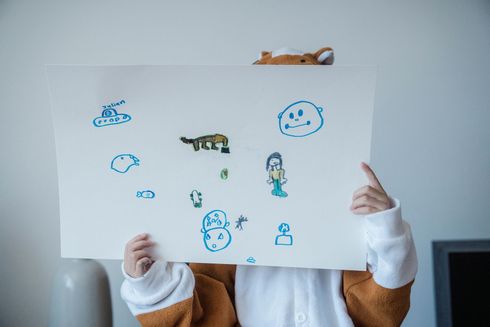 Person holding a white poster with childlike blue and green doodles and a small fox drawing on top
