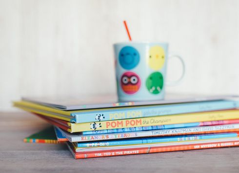 Colorful mug with smiley faces stacked on books against a white background