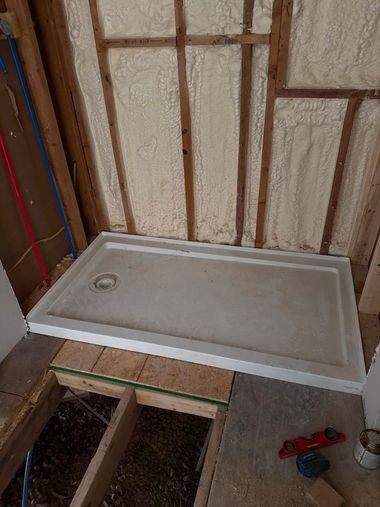 Bathroom under construction with a white shower base, exposed wall studs, and tools on the floor.