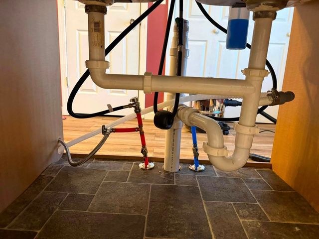 Under-sink plumbing and pipes inside a cabinet with visible valves and floor tiles