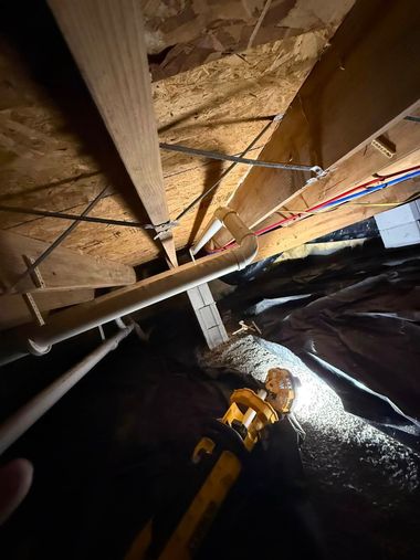Looking up inside a dim attic with wooden beams, wiring, and insulation around an opening.