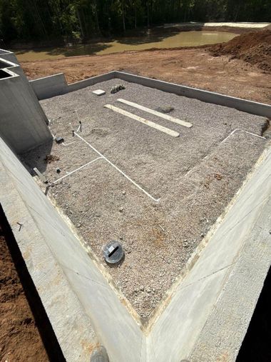 Concrete utility pit with gravel bed, white pipes, and a surrounding retaining wall outdoors.