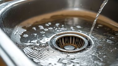 Water pouring into a stainless steel sink drain, creating ripples around the strainer.