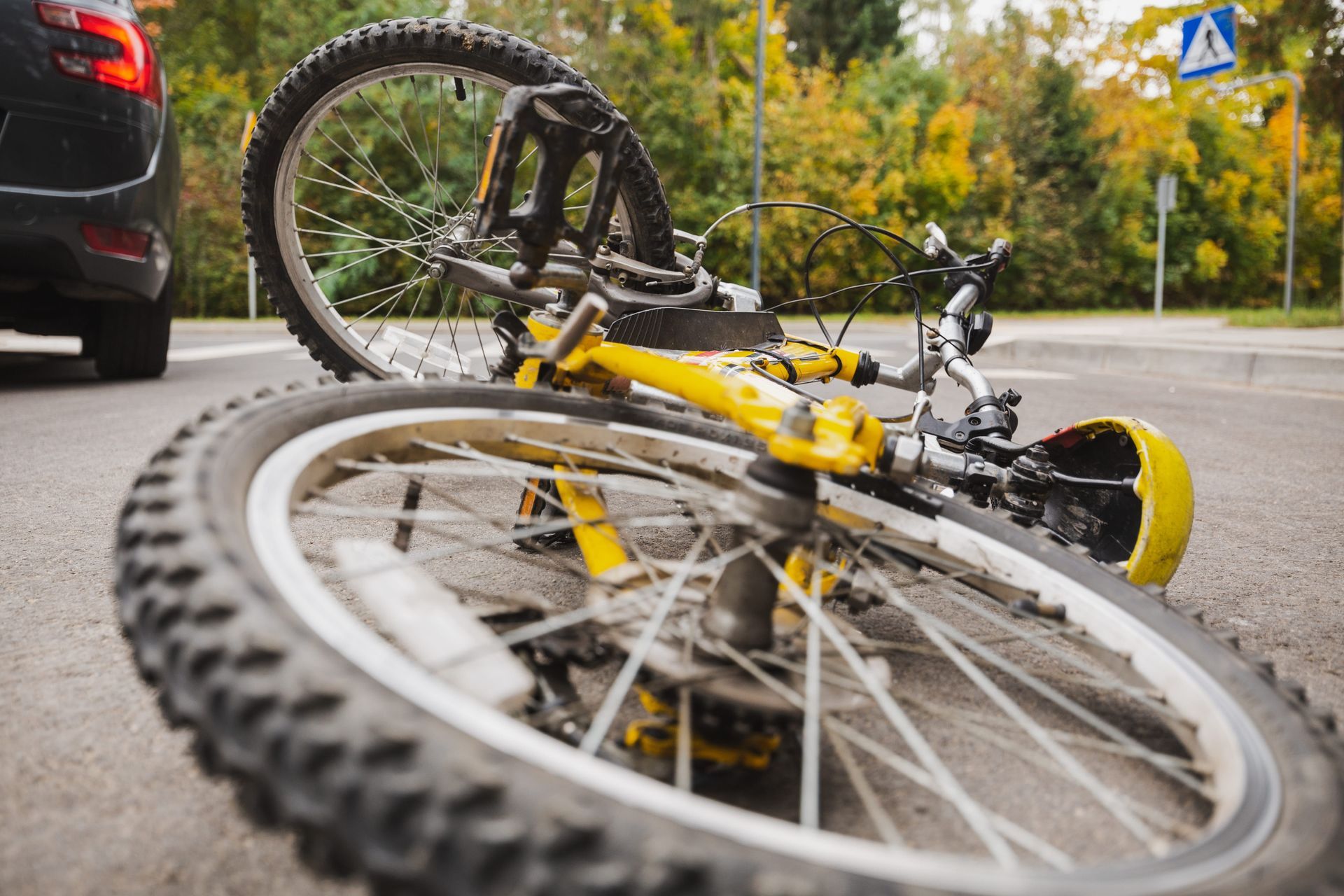 Yellow bicycle lying on its side in the road near a car and autumn trees
