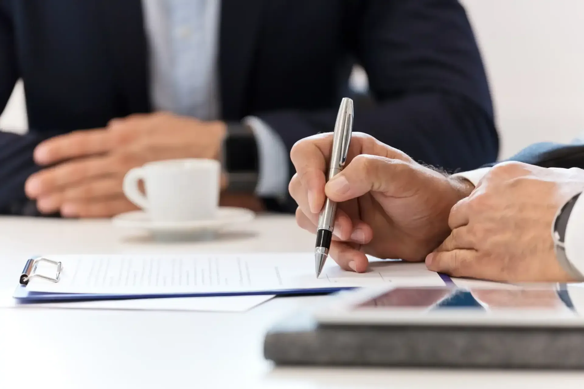 Hands signing a document at a business meeting with a coffee cup on the table