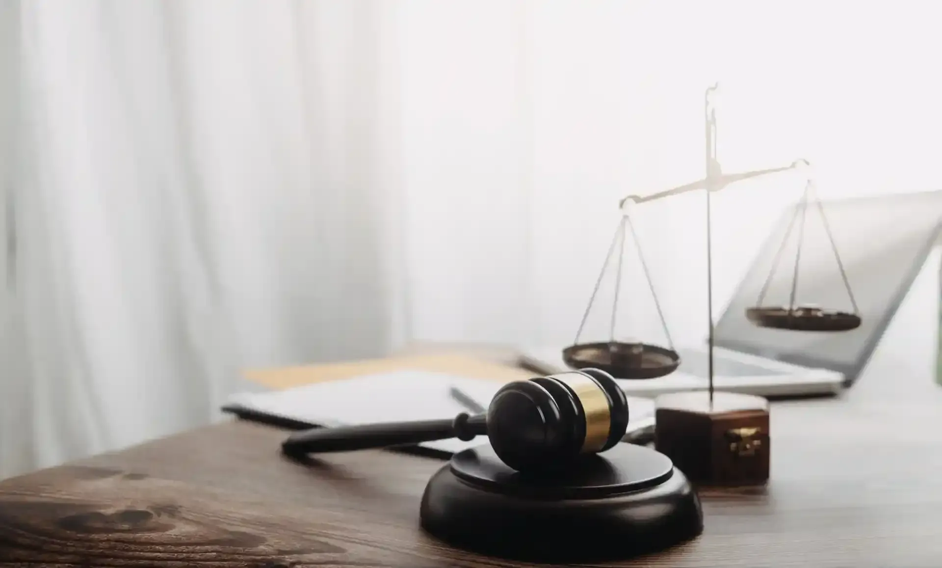 Judge’s gavel, scales of justice, and wooden block on a desk beside a small hourglass.