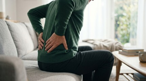 Person holding lower back while sitting on a couch in a bright living room