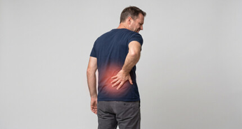 Man holding his lower back in pain, standing against a plain gray background.