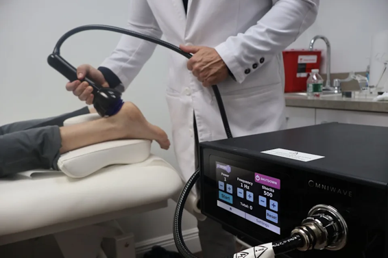 Clinician using a handheld device on a patient’s leg beside a medical treatment machine
