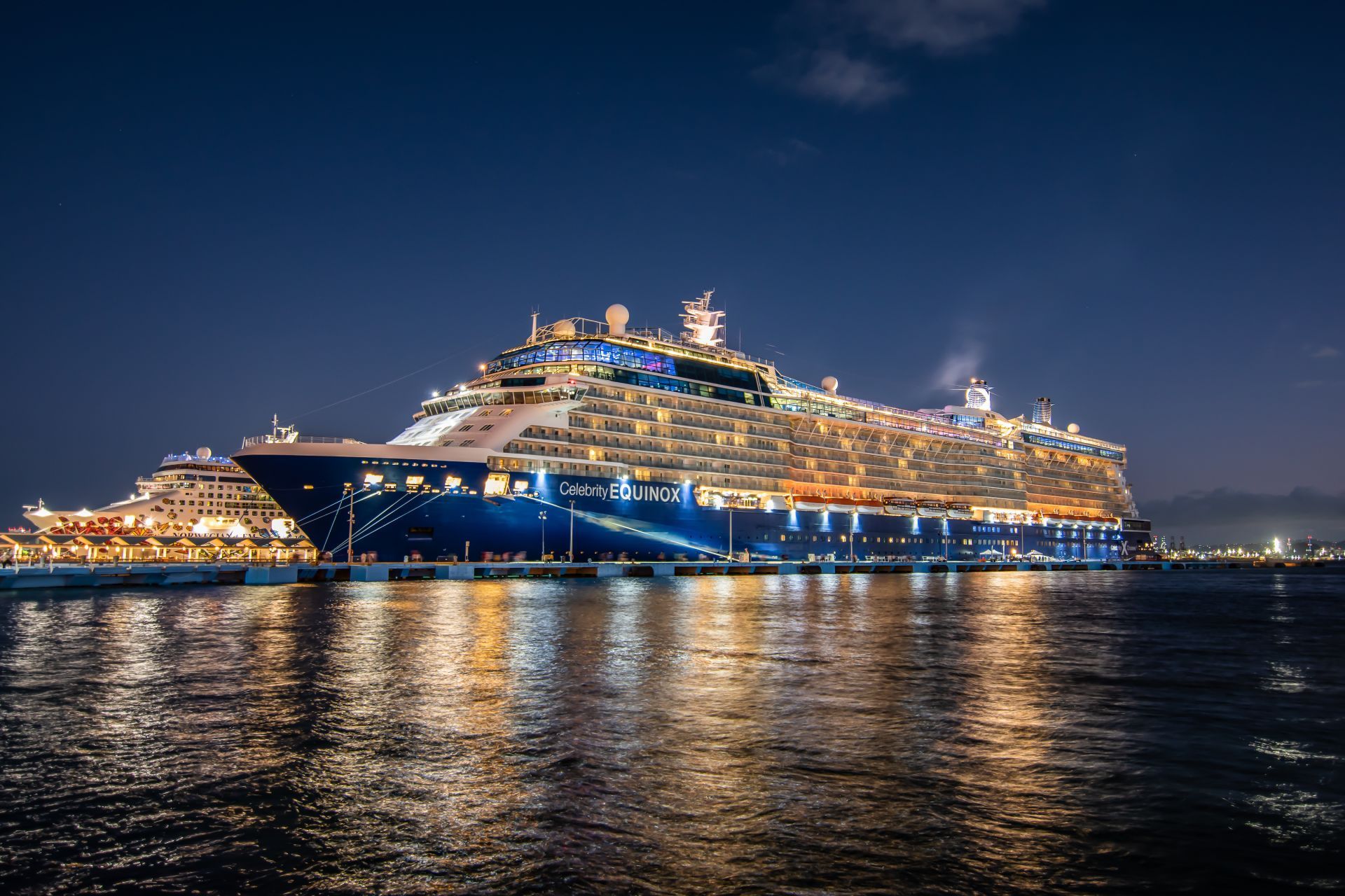 A large, dark blue cruise ship docked at night; lights reflect on the water.