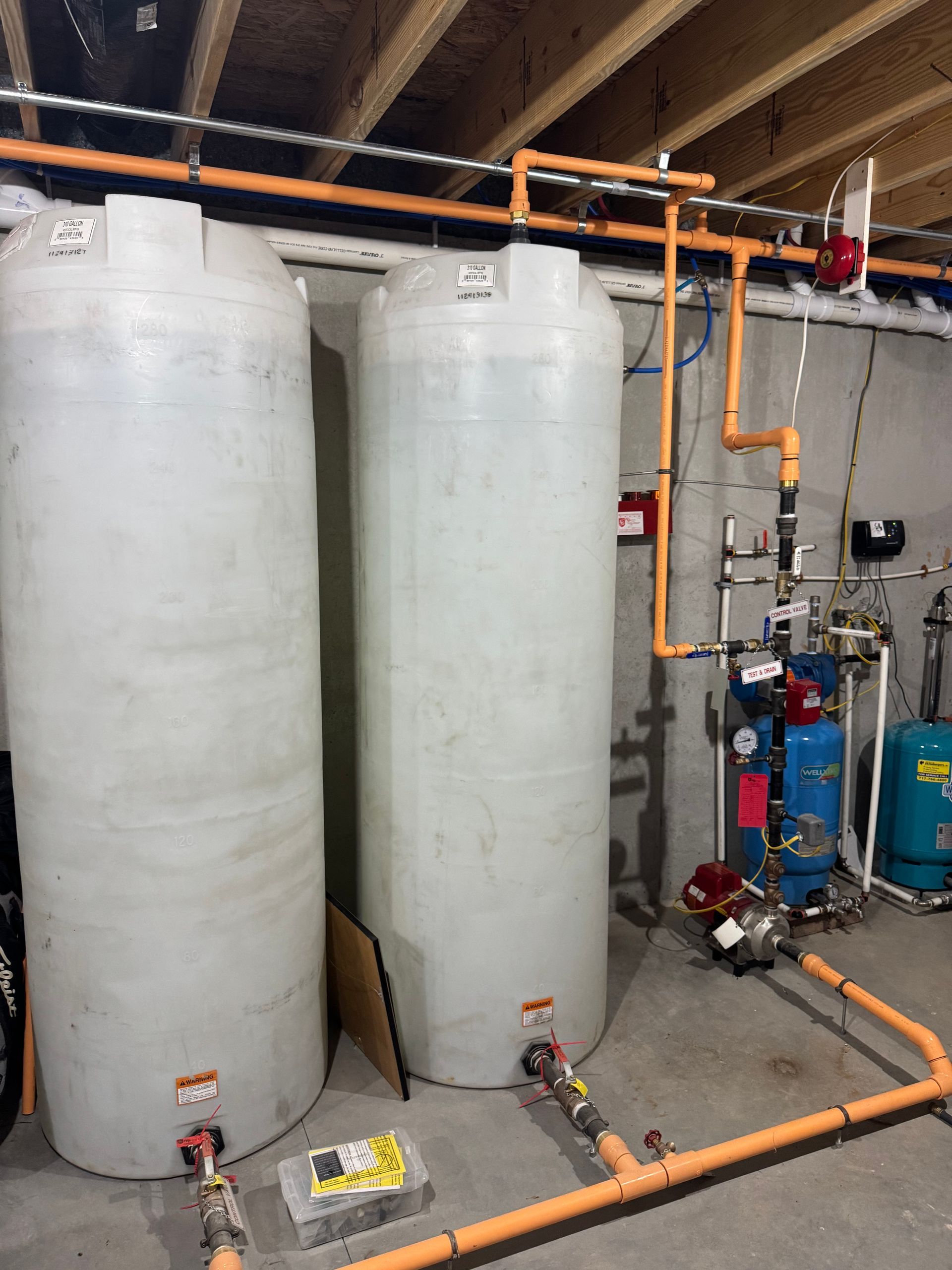 Two large water tanks with orange pipes in a basement.