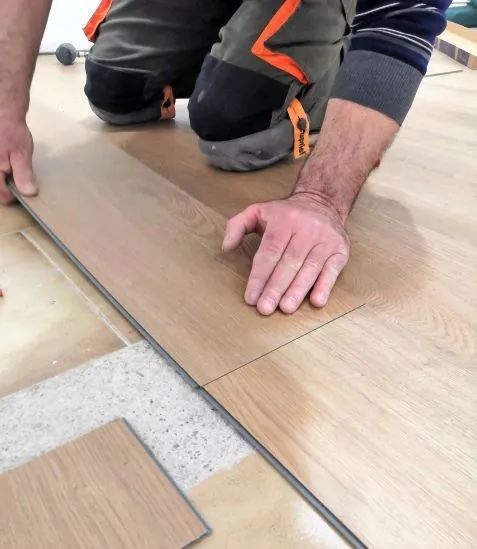 Persona che installa un pavimento effetto legno, inginocchiata sul pavimento, che posiziona un'asse.