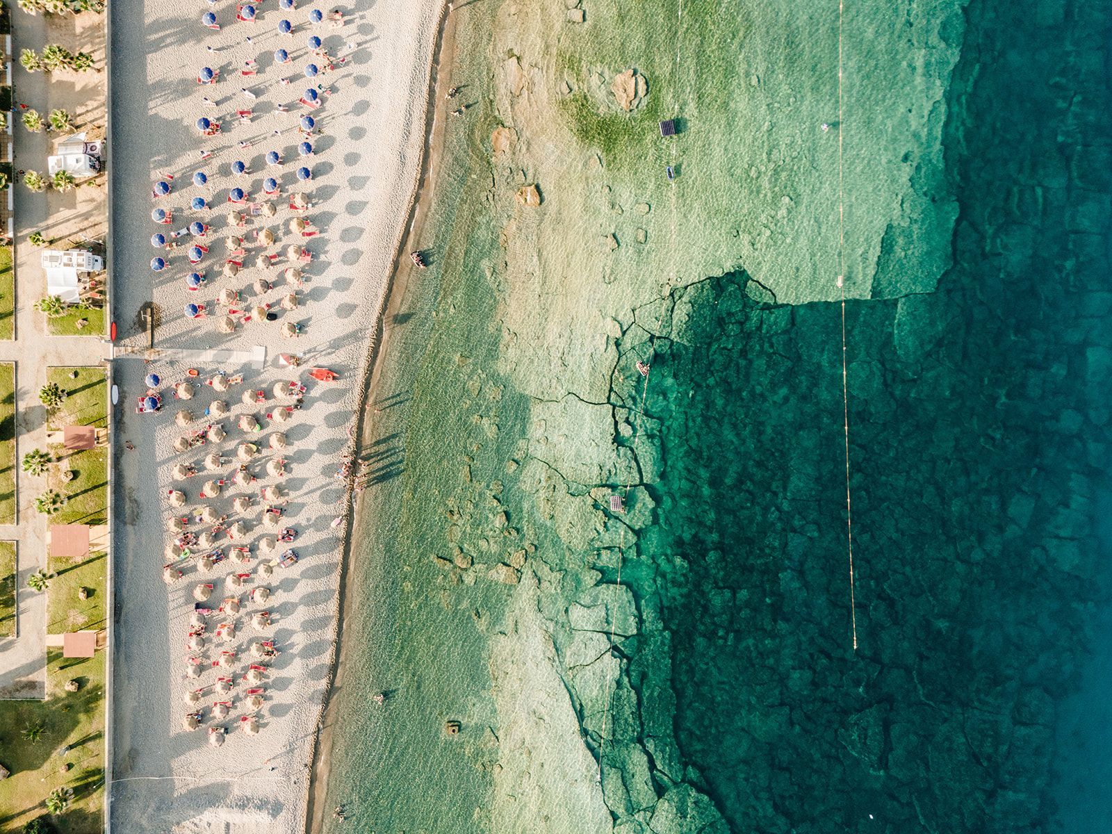 Vista aerea della spiaggia con ombrelloni, persone e acqua turchese e limpida.