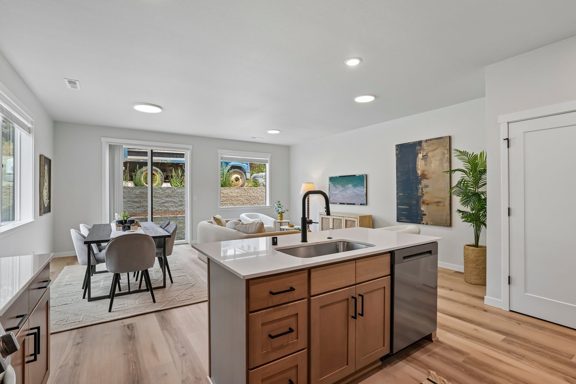 Bright open kitchen and dining area with island, white walls, wood floors, and large windows