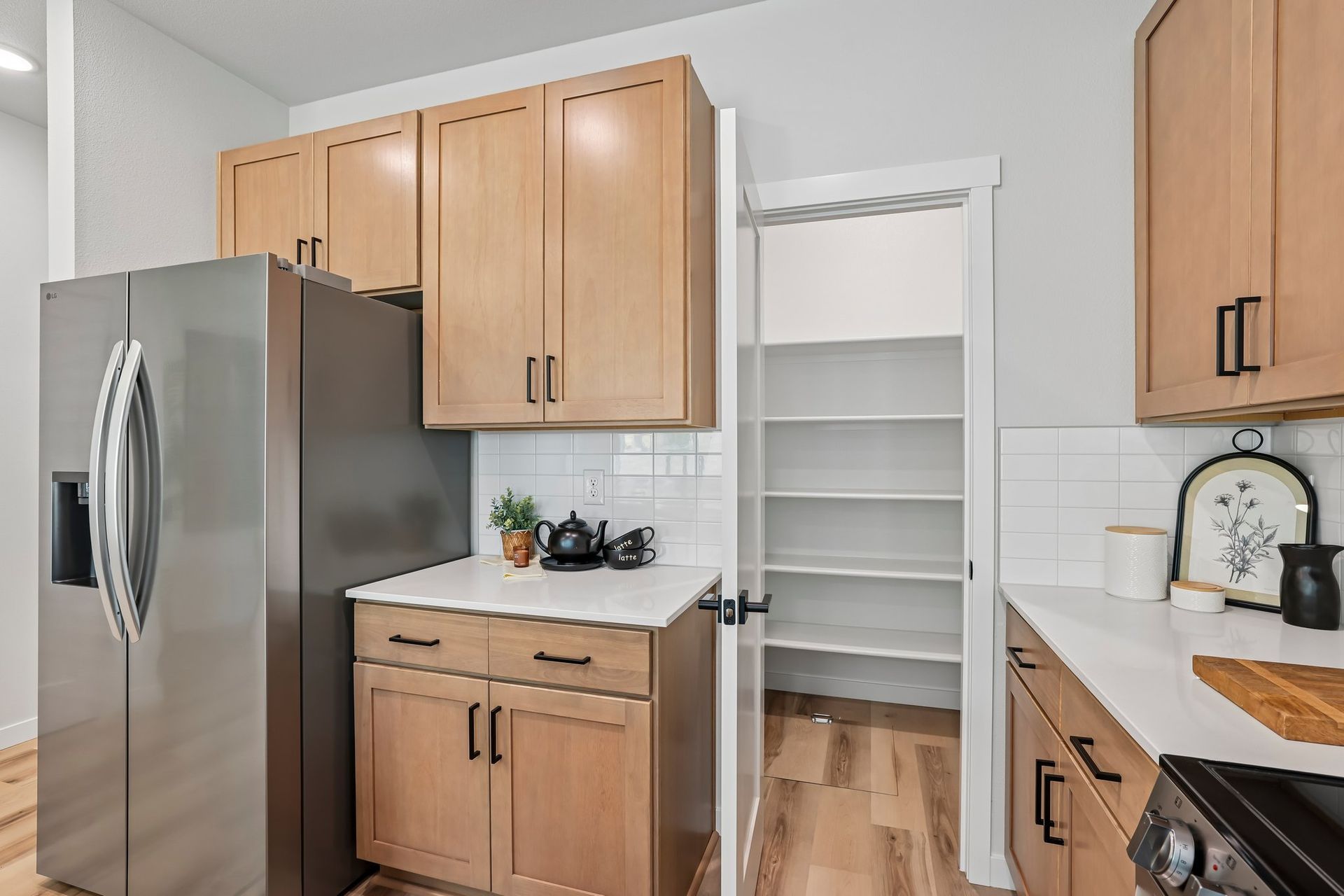 Bright kitchen with stainless fridge, wood cabinets, white shelving pantry, and hardwood floor.
