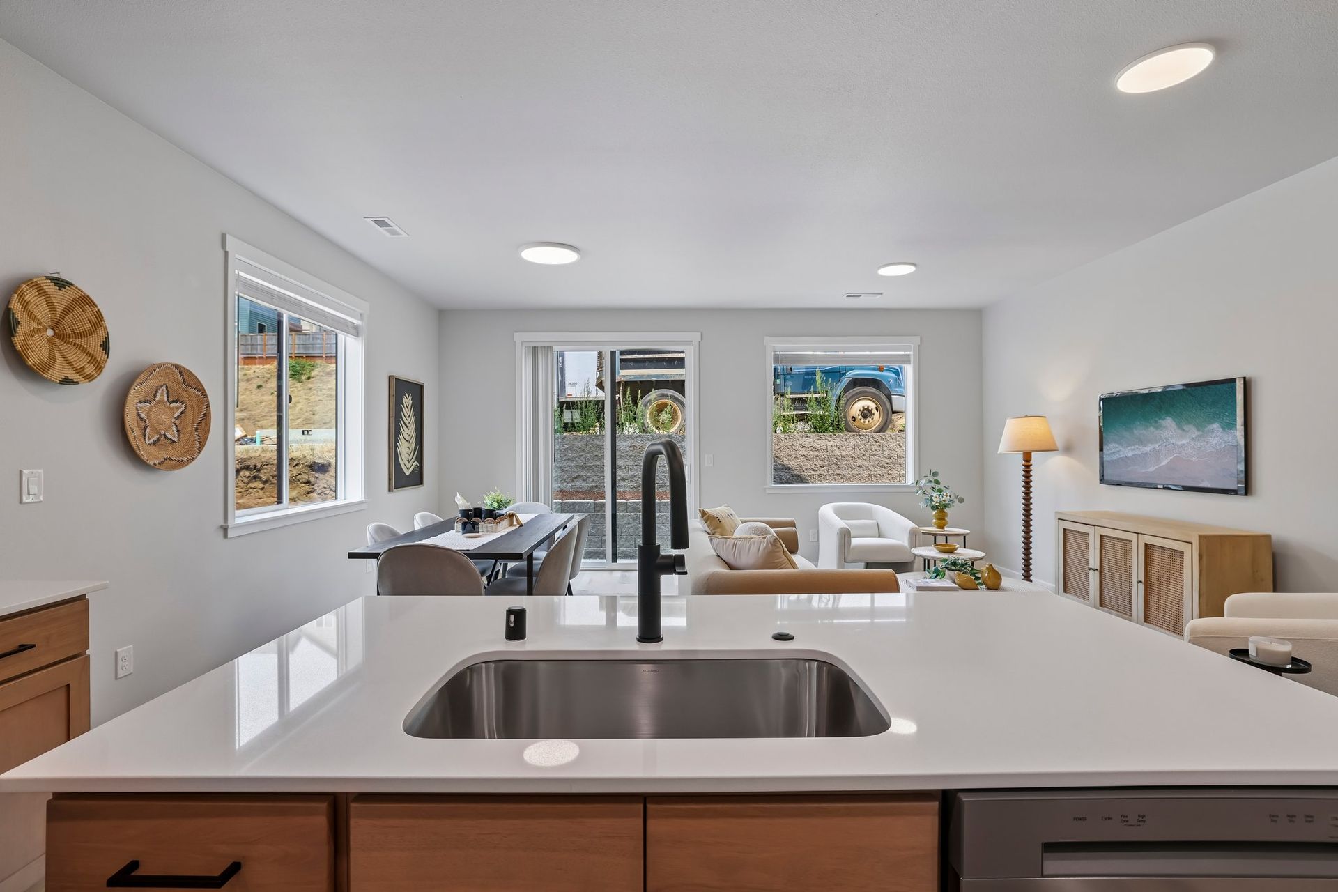 Bright modern kitchen and living area with white island, stainless sink, and ocean-view windows