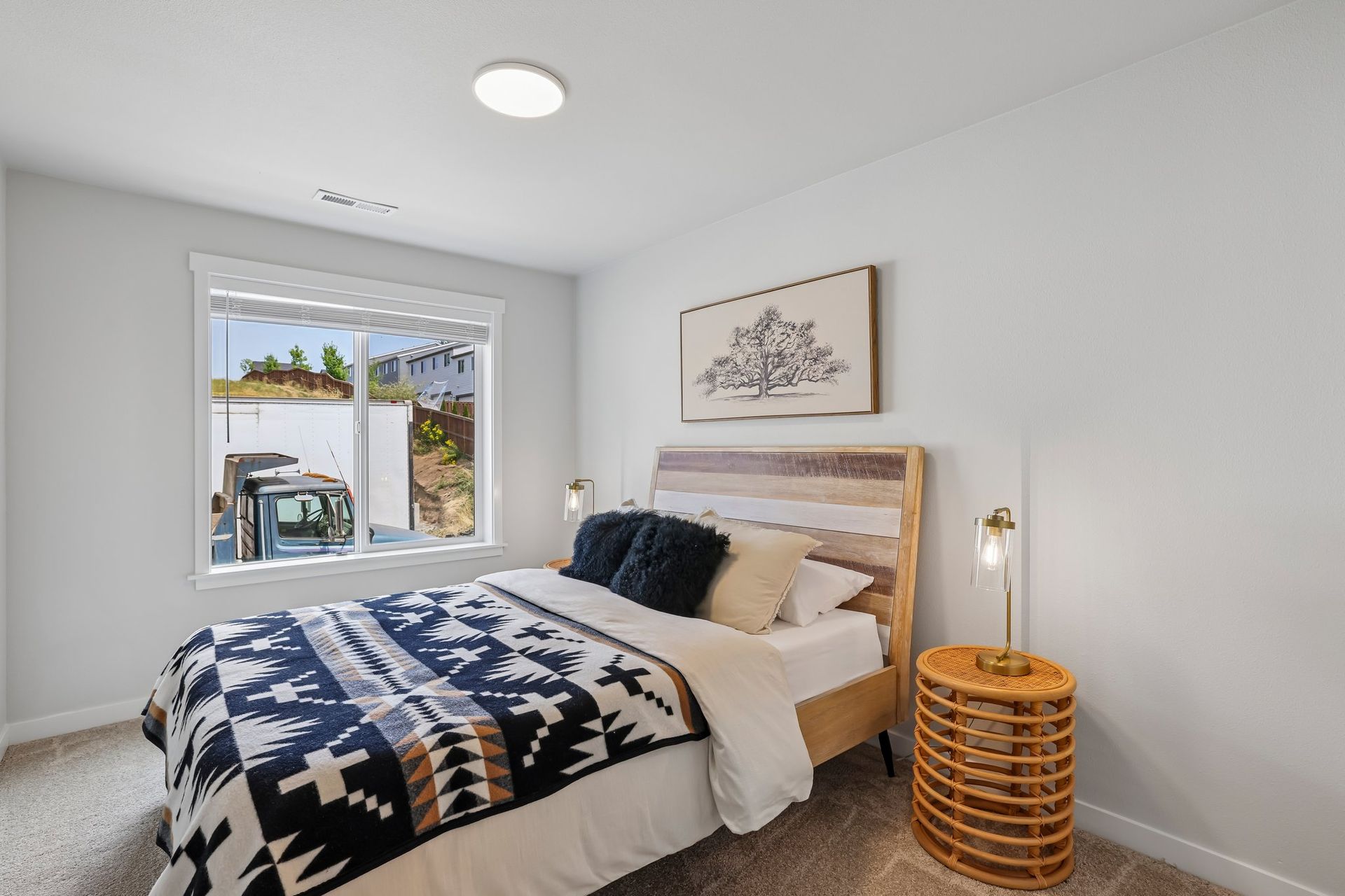 Bright minimalist bedroom with bed, woven side table, wall art, and window view to patio