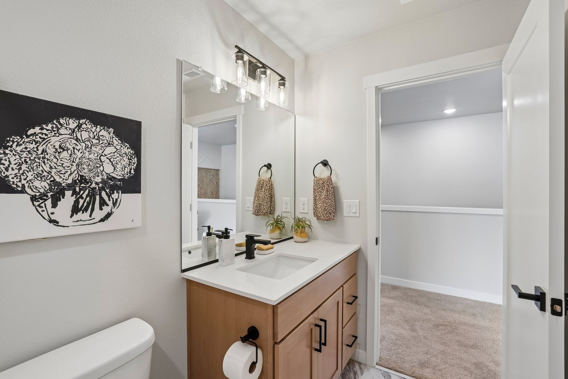 Bright bathroom vanity with mirror, sink, white walls, and open doorway to a carpeted room.