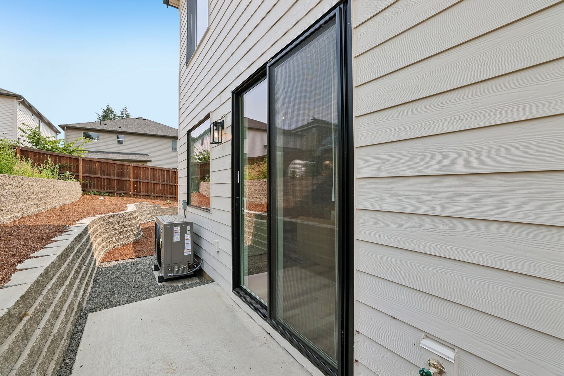 Narrow concrete patio beside a house with sliding glass doors, air conditioner, and fenced yard.