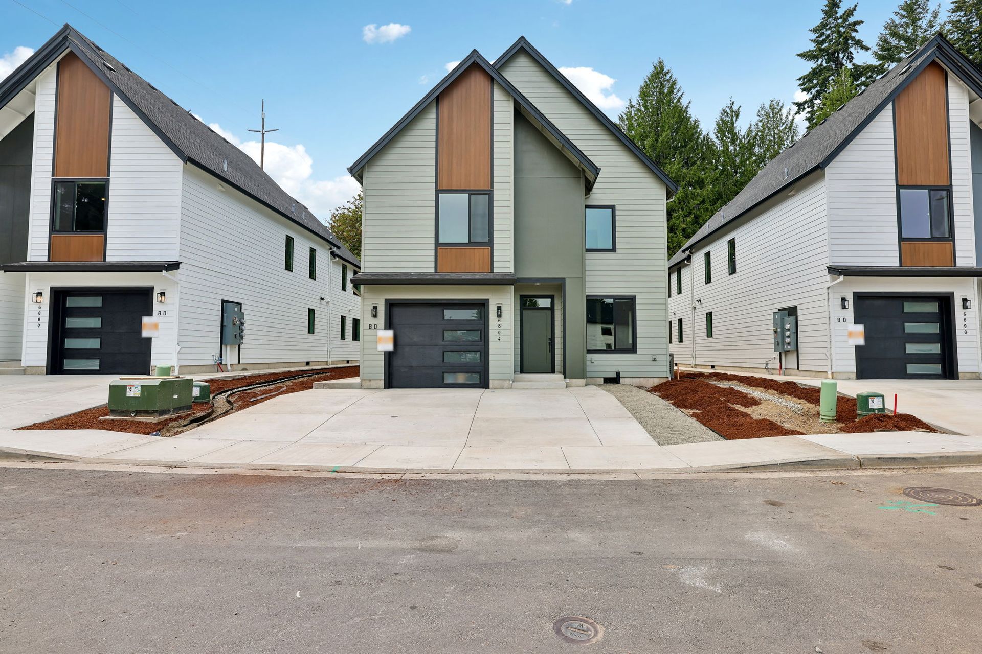 Three modern white duplex homes with black garages and wooden accents along a quiet street