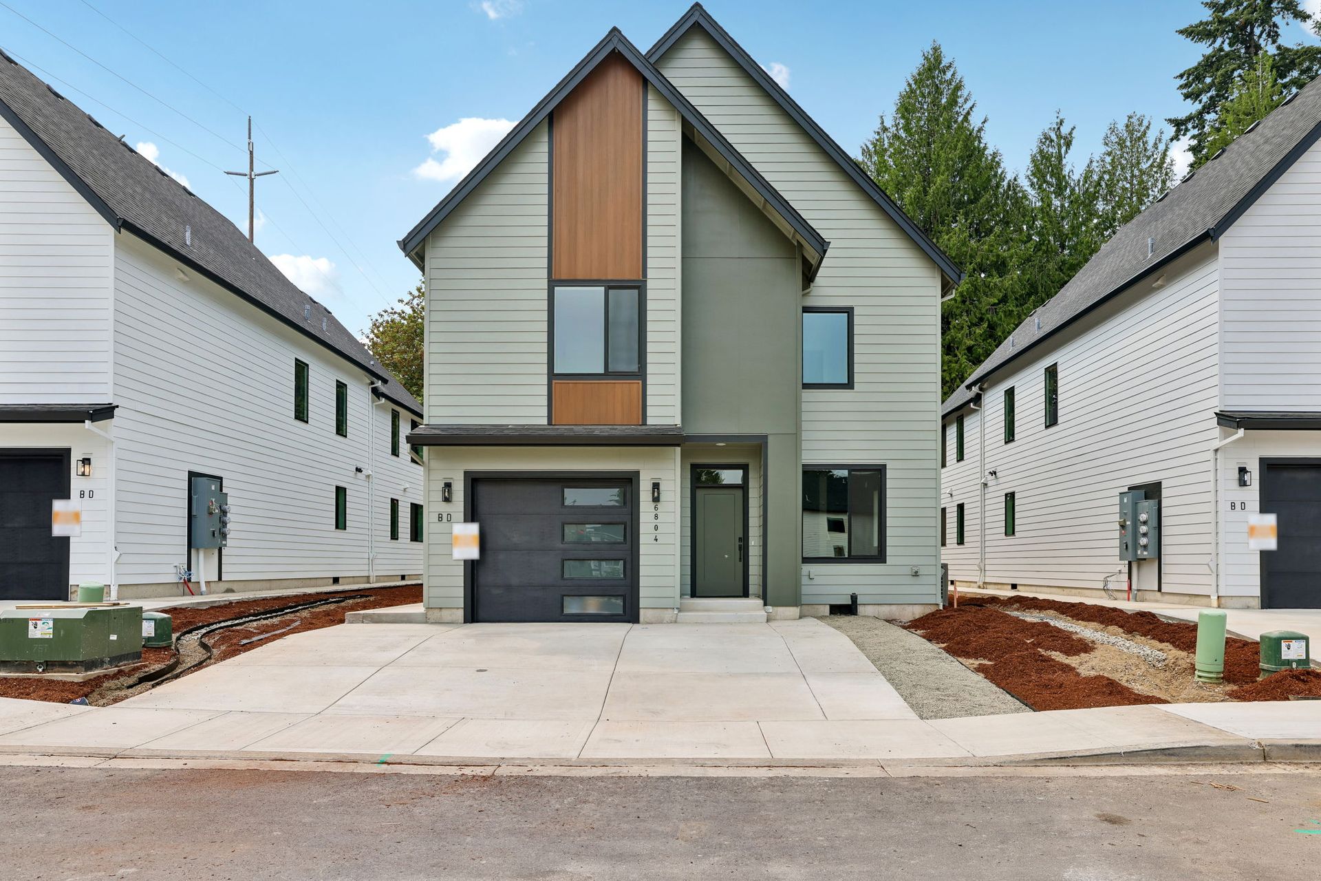 Modern two-story house with gray siding, wood accents, and a garage, flanked by similar homes on a quiet street