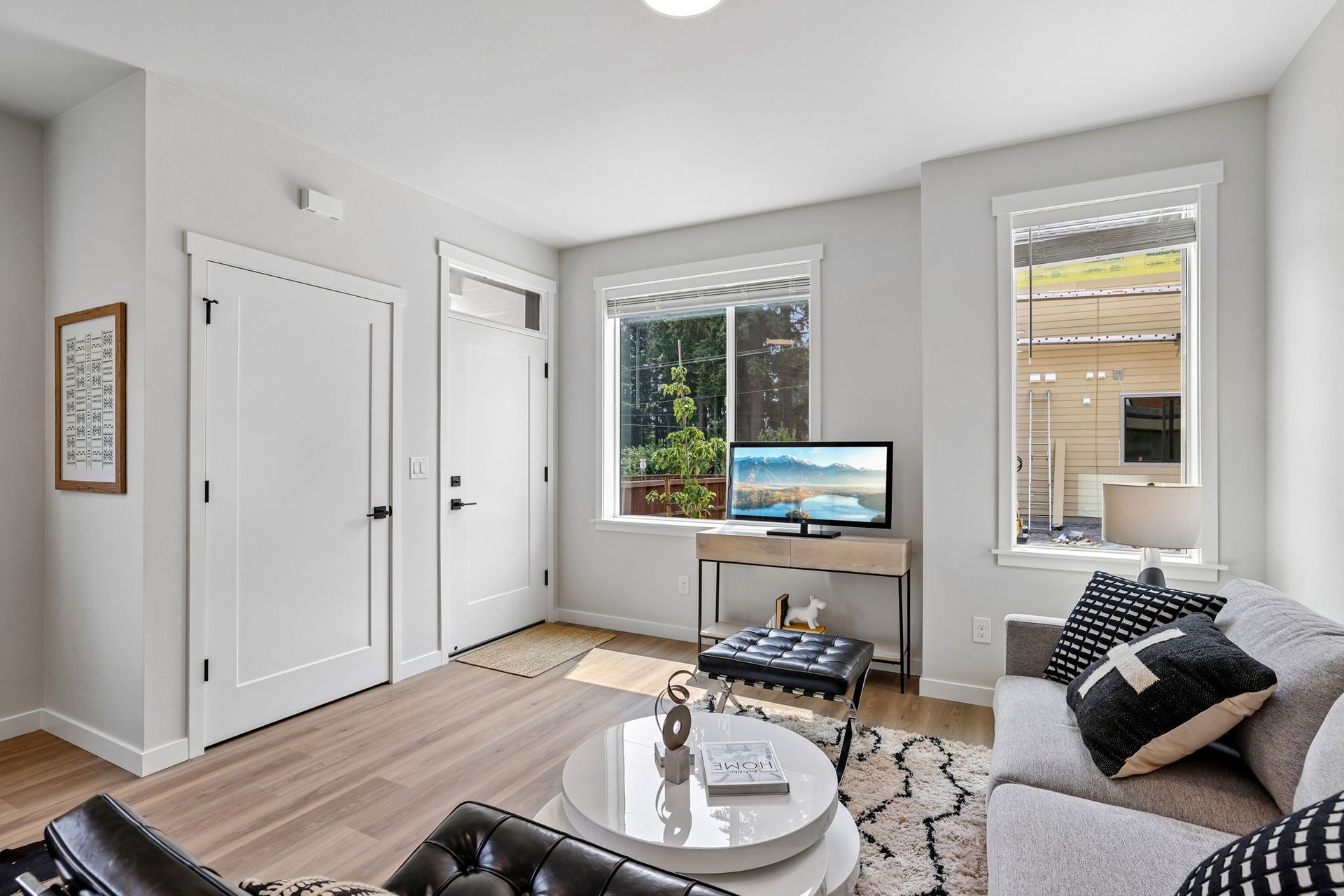 Bright living room with gray sofa, TV on stand, coffee table, windows, and white doors on light wood floors