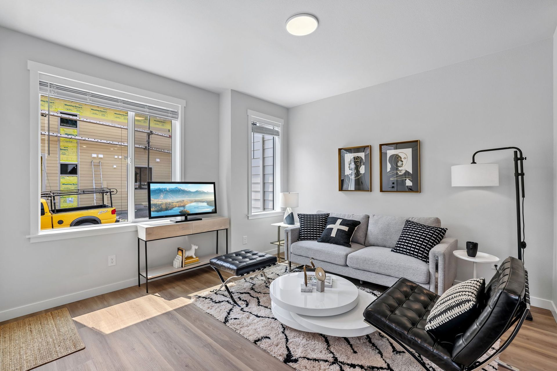 Bright modern living room with gray sofa, round coffee table, TV, fireplace, and large windows
