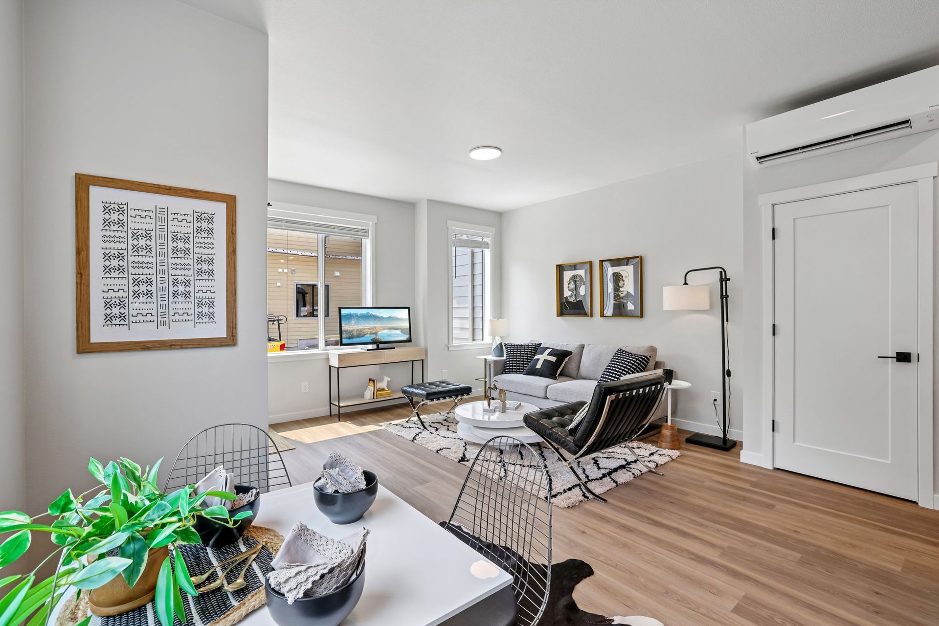 Bright modern living room with white walls, wood floors, black chairs, desk, and potted plants