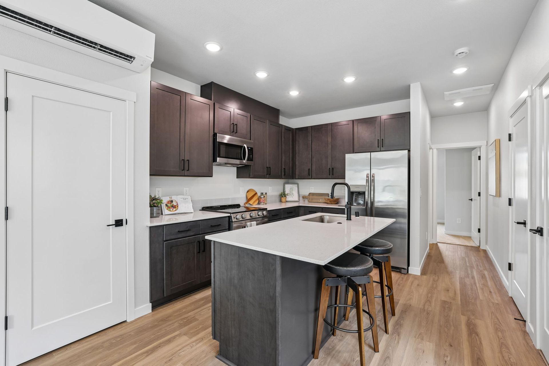 Modern white kitchen with dark cabinets, large island, bar stools, and hardwood floors