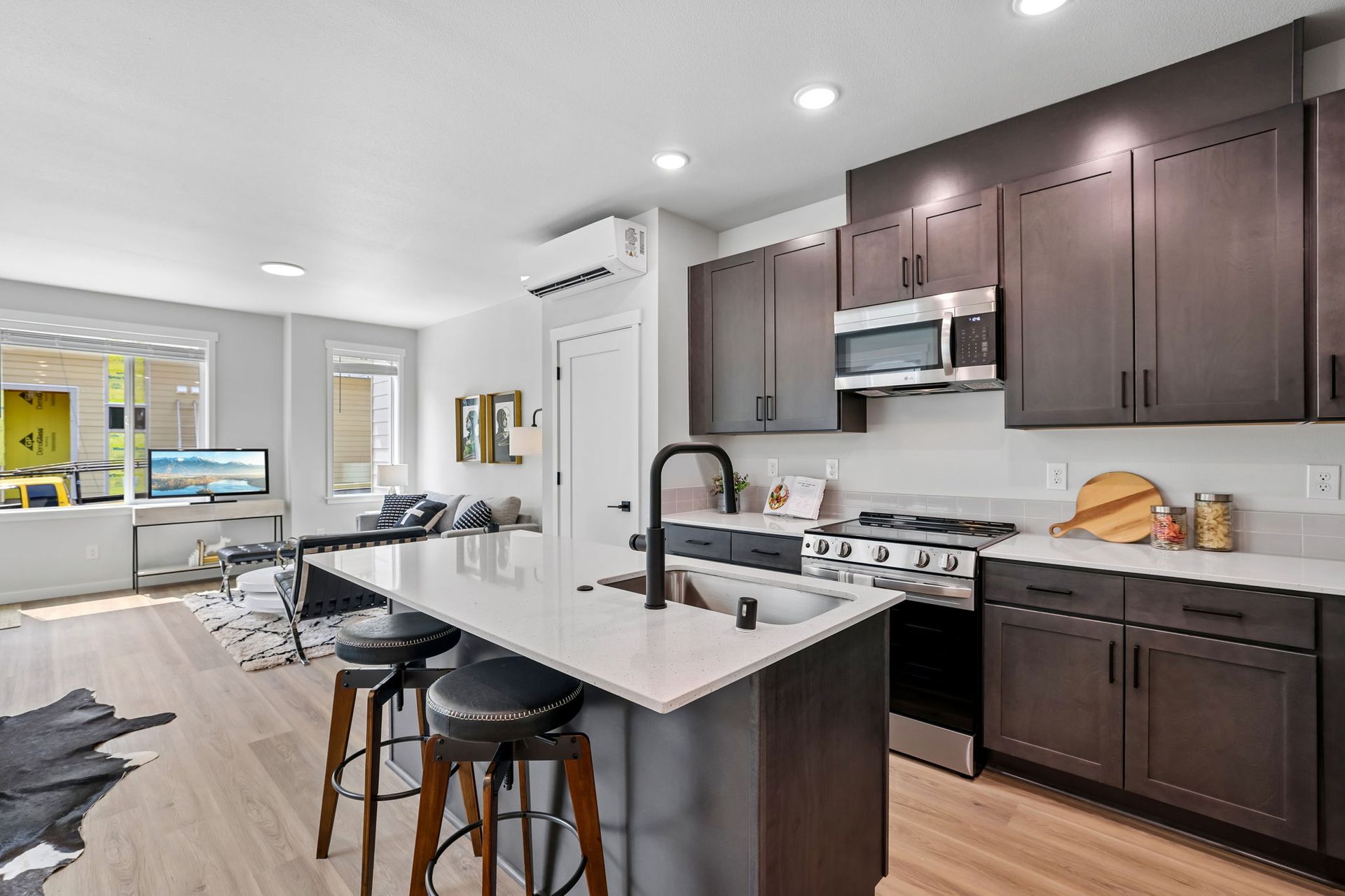 Bright modern kitchen with dark cabinets, white island, bar stools, and open living area beyond