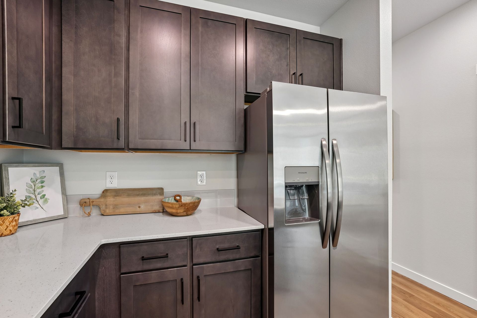 Modern kitchen corner with dark wood cabinets, white countertops, and stainless steel refrigerator