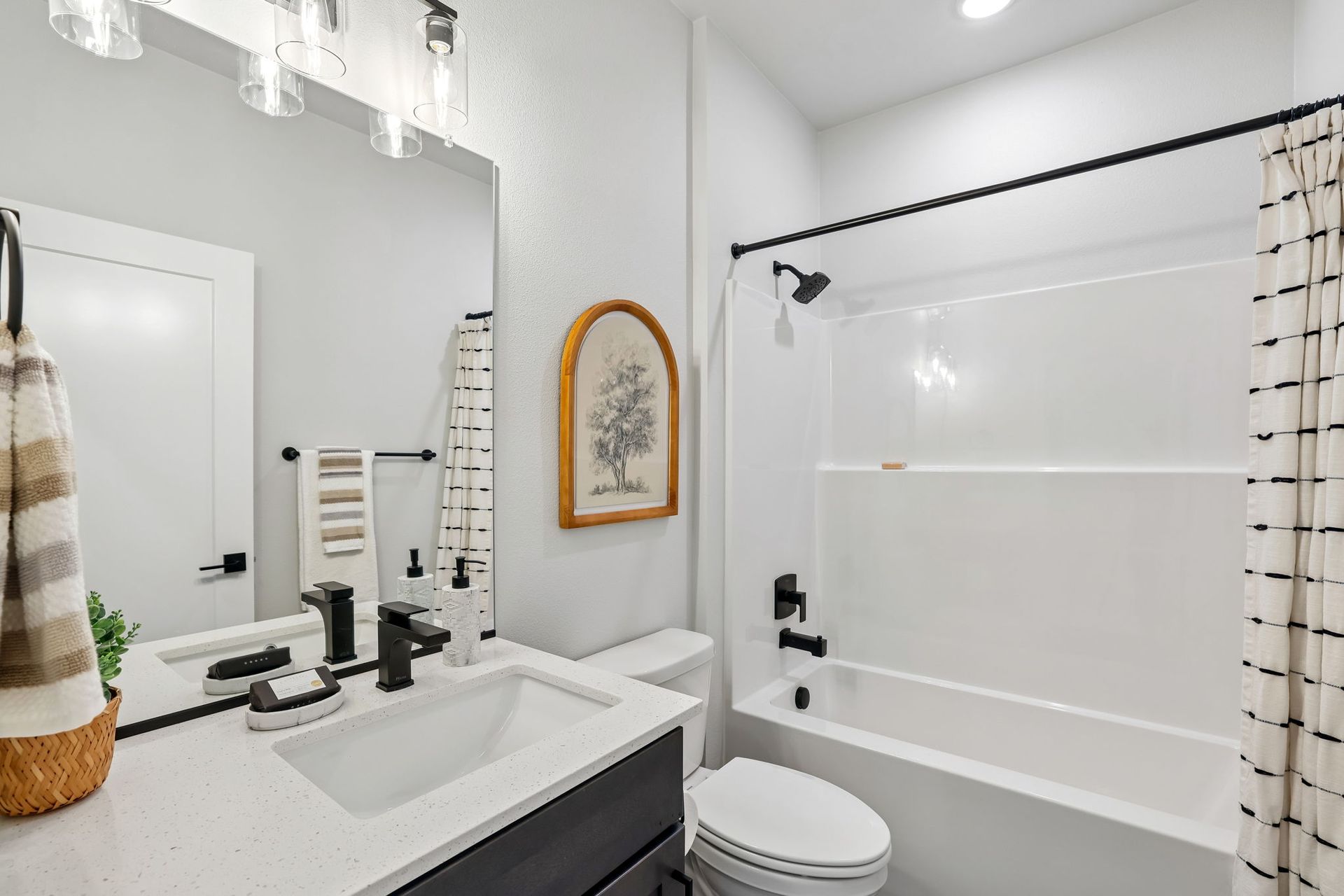 Bright white bathroom with vanity, mirror, toilet, and tub with shower curtain