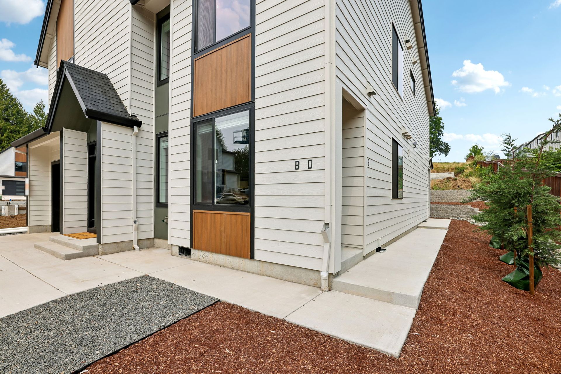 Modern townhouse exterior with white siding, wood accents, front walkway, and landscaped yard