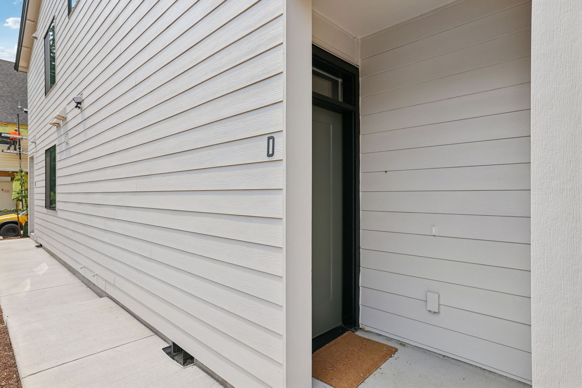 Modern white-sided building exterior with a narrow side entrance and concrete walkway