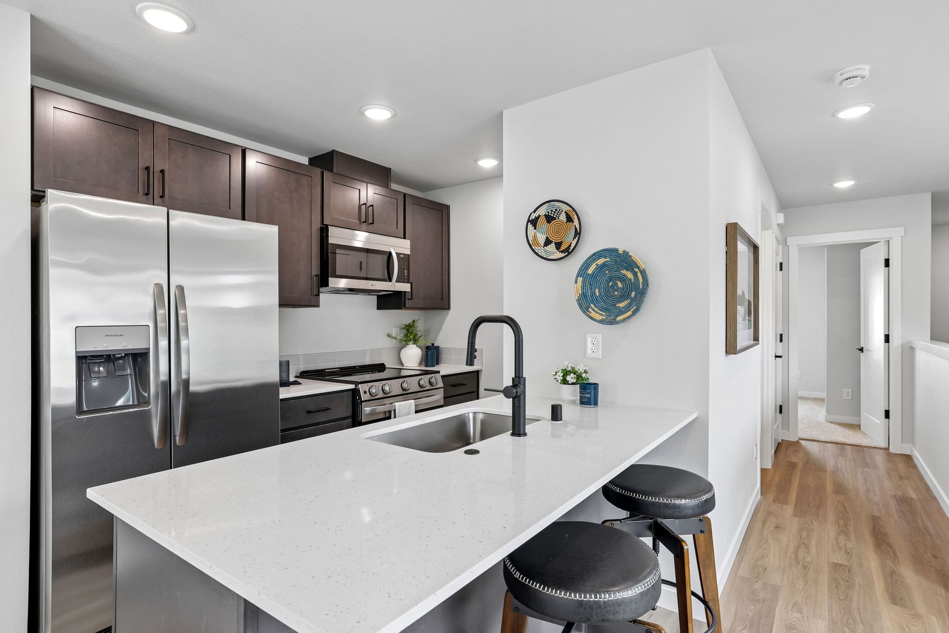 Modern kitchen with stainless steel appliances, white island, dark cabinets, and light wood floors