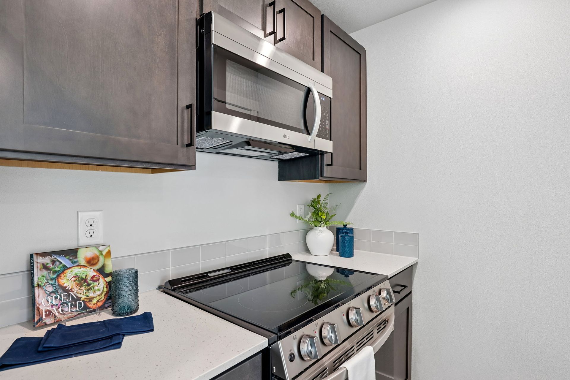 Modern kitchen corner with stainless steel stove and microwave, gray cabinets, and light countertops.