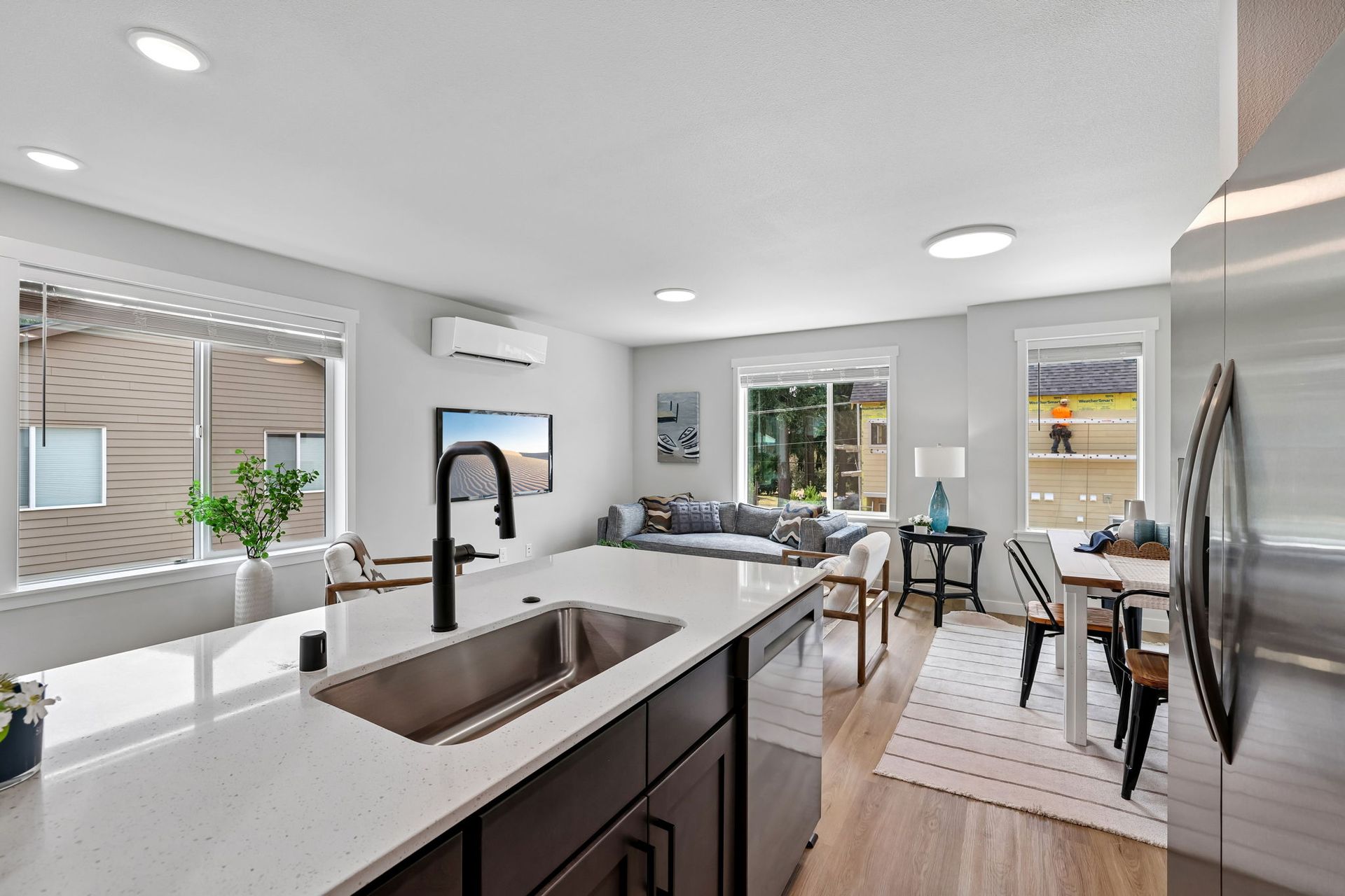 Bright modern kitchen and living area with island sink, white cabinets, wood floors, and large windows