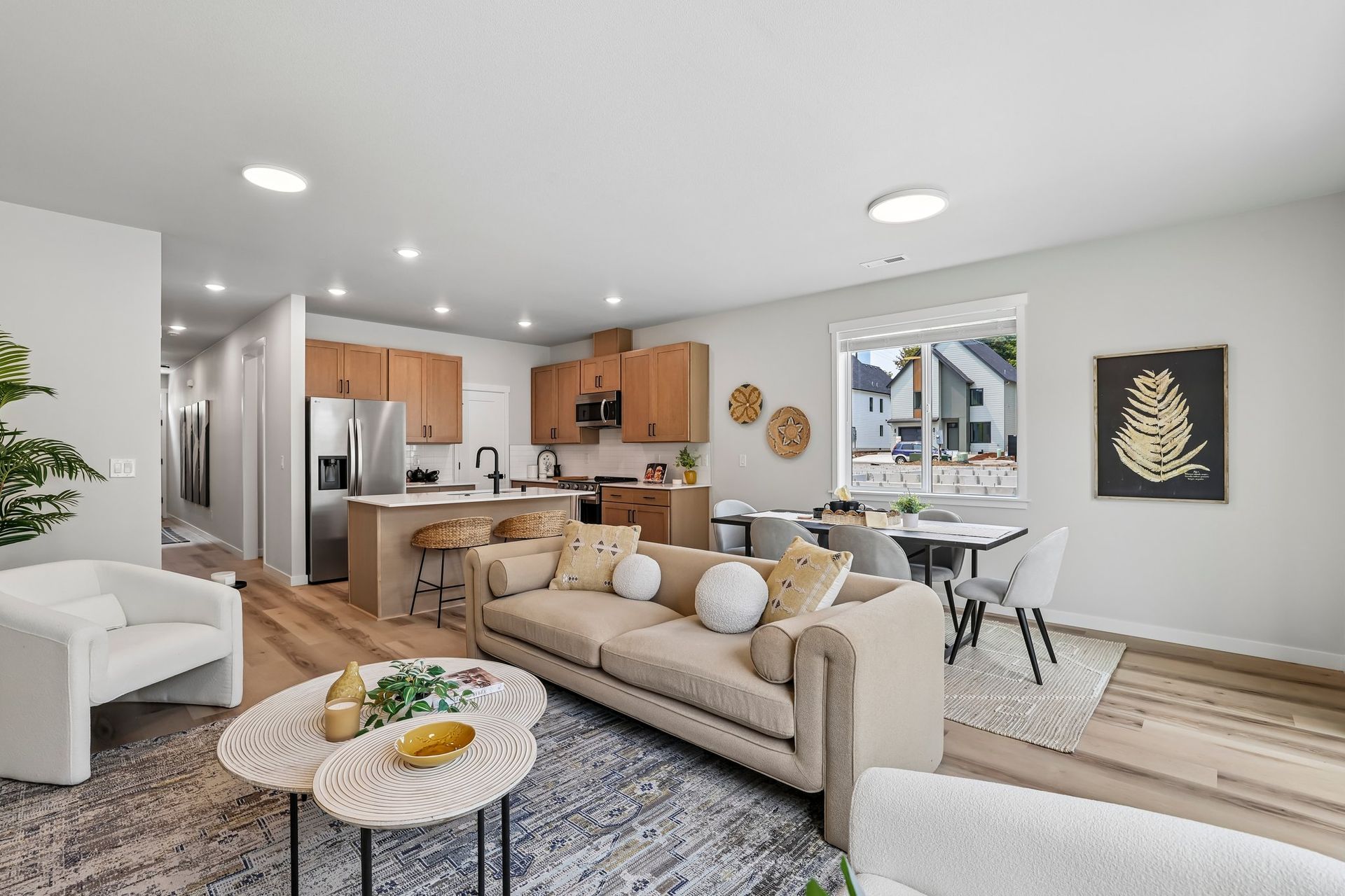 Bright modern open-plan living room with beige sofa, dining area, kitchen, and wall art