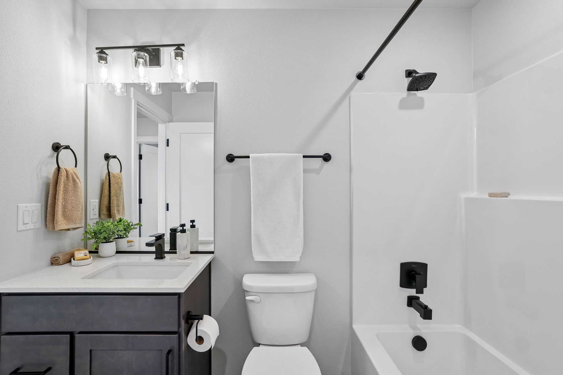 Bright white bathroom with vanity, toilet, shower, and black fixtures