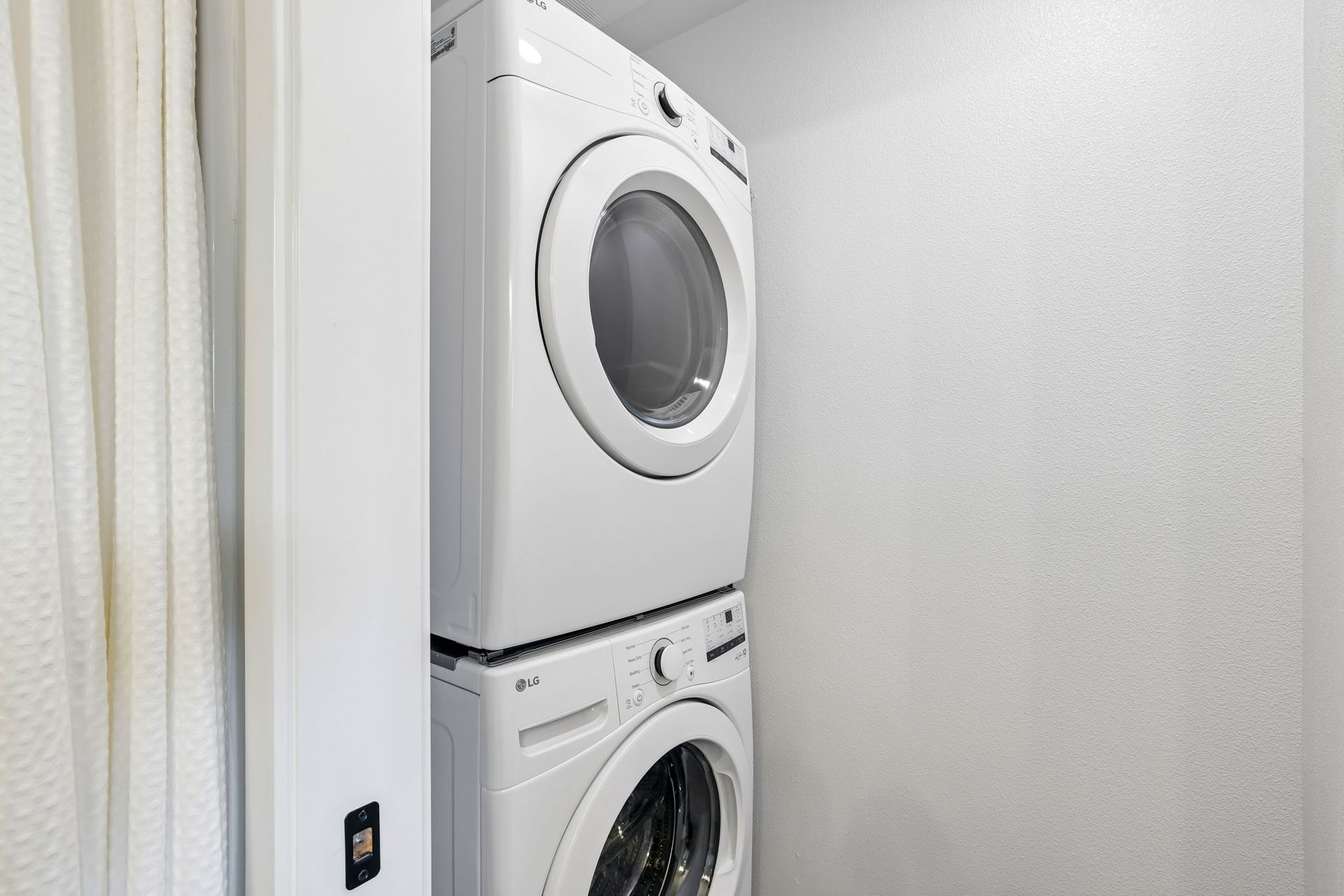 Stacked white washer and dryer in a narrow laundry closet