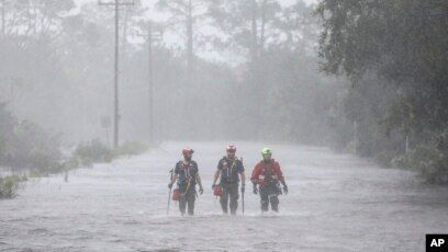 Three people are walking through a flooded road.