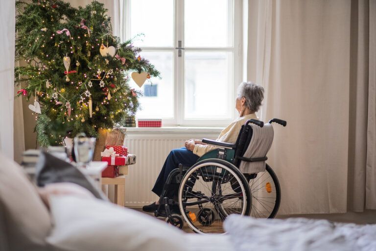 An elderly woman in a wheelchair is sitting in front of a christmas tree.